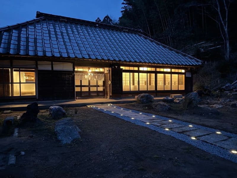 夜の母屋と、灯りが並ぶ石畳の小径